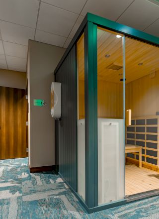 A modern sauna with glass doors is in a room featuring lockers, a bench, and calming decor.